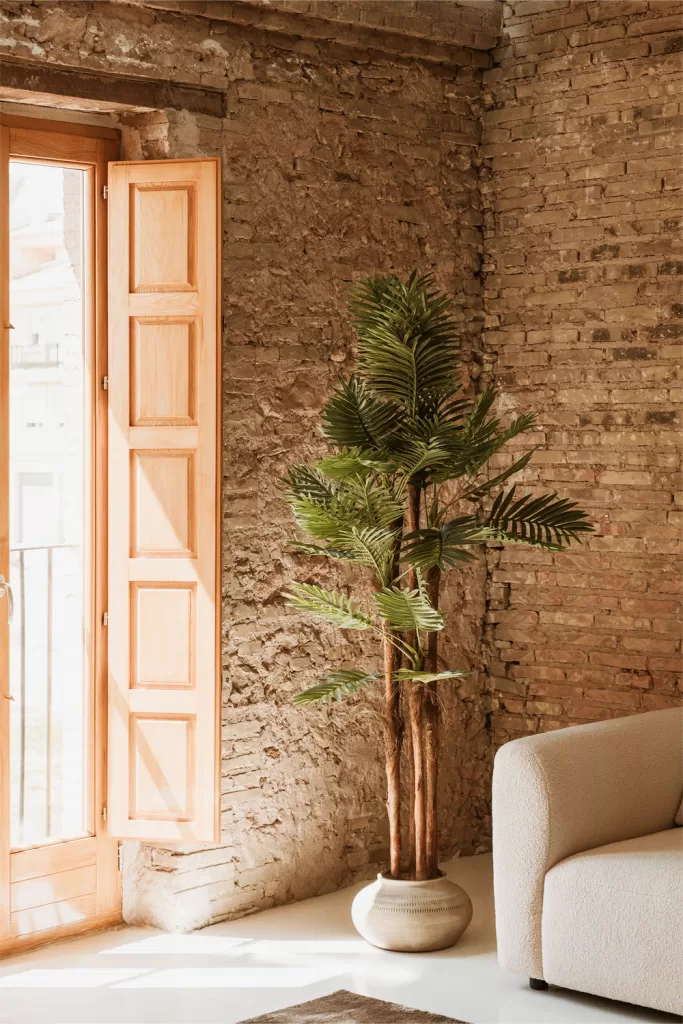 Planta alta junto a sofá beige y pared de ladrillo en salones marrones y beige con vegetación