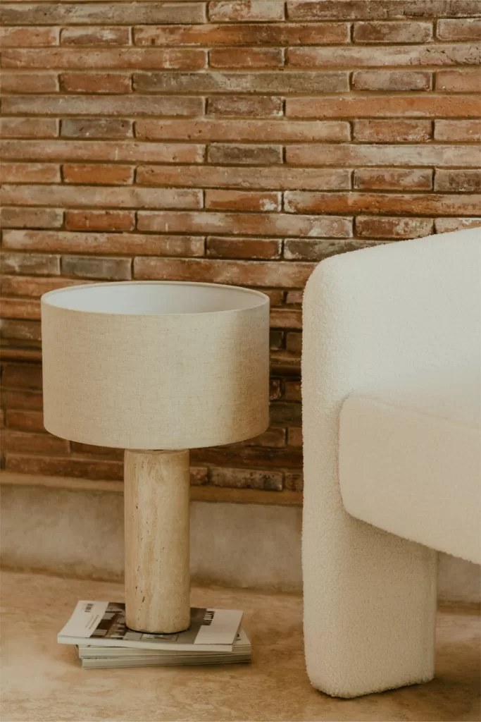 Lámpara de sobremesa beige con base de madera junto a sofá blanco para Iluminar un salón acogedor
