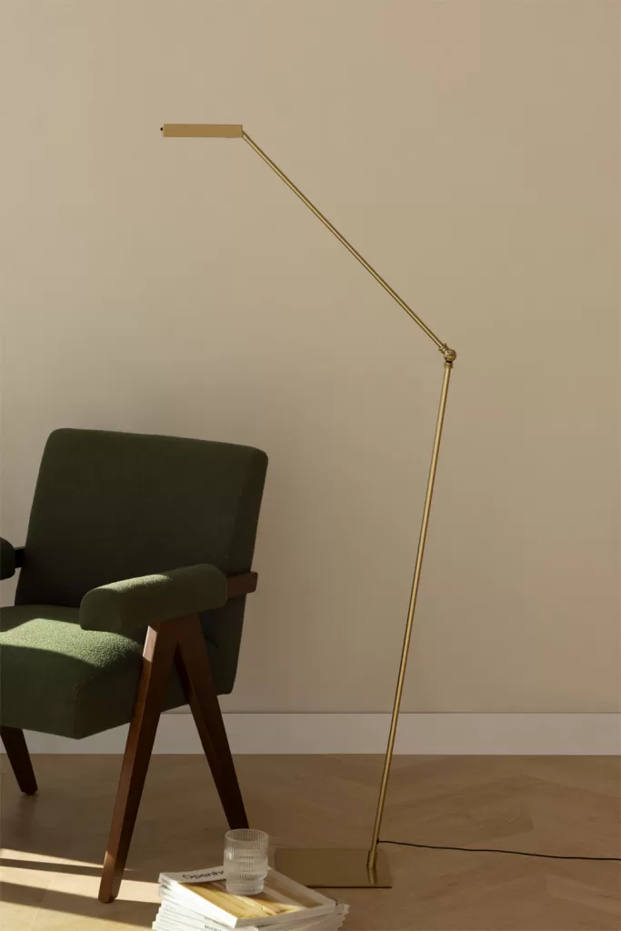 Cantinho de leitura com uma poltrona elegante e um candeeiro de pé articulado em metal dourado.