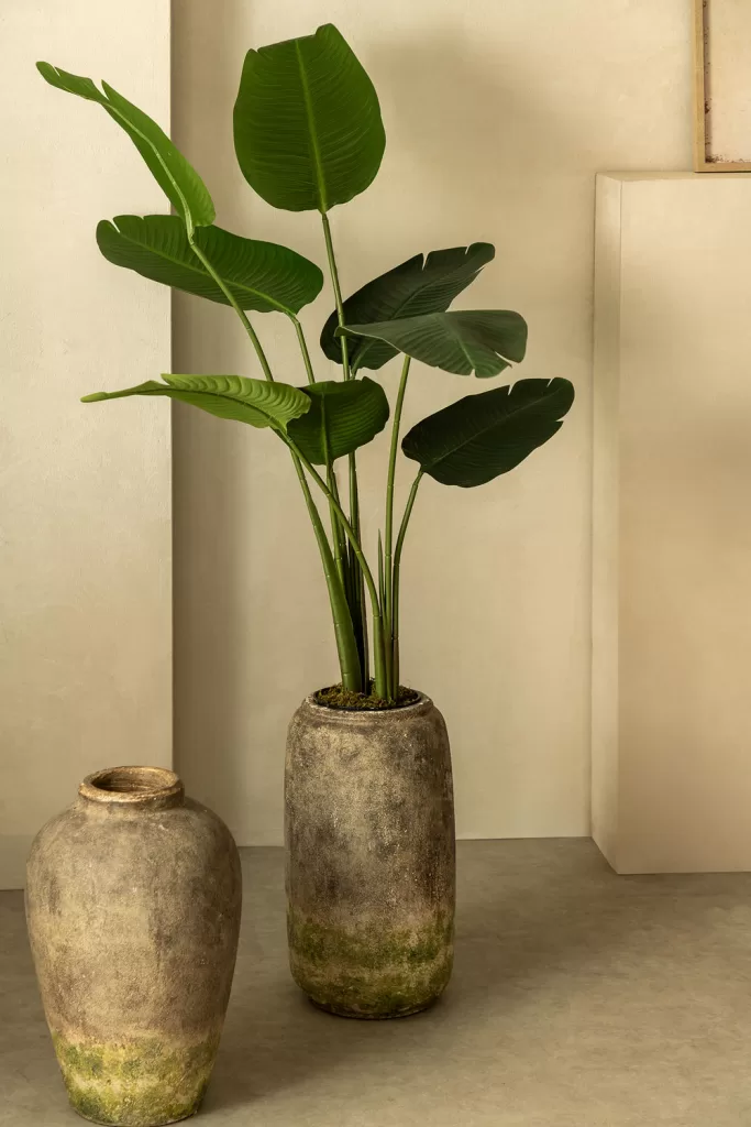 Detalhe de um cantinho de leitura decorado com uma planta artificial verde exuberante num vaso elegante.