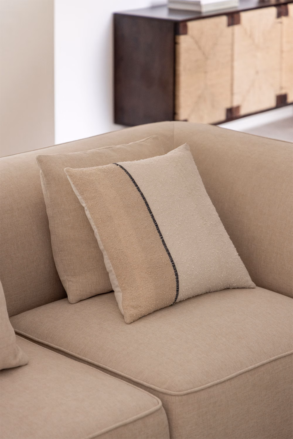 Coussins carrés et rectangulaires superposés dans des tons sable sur un canapé beige, montrant comment jouer avec les volumes.