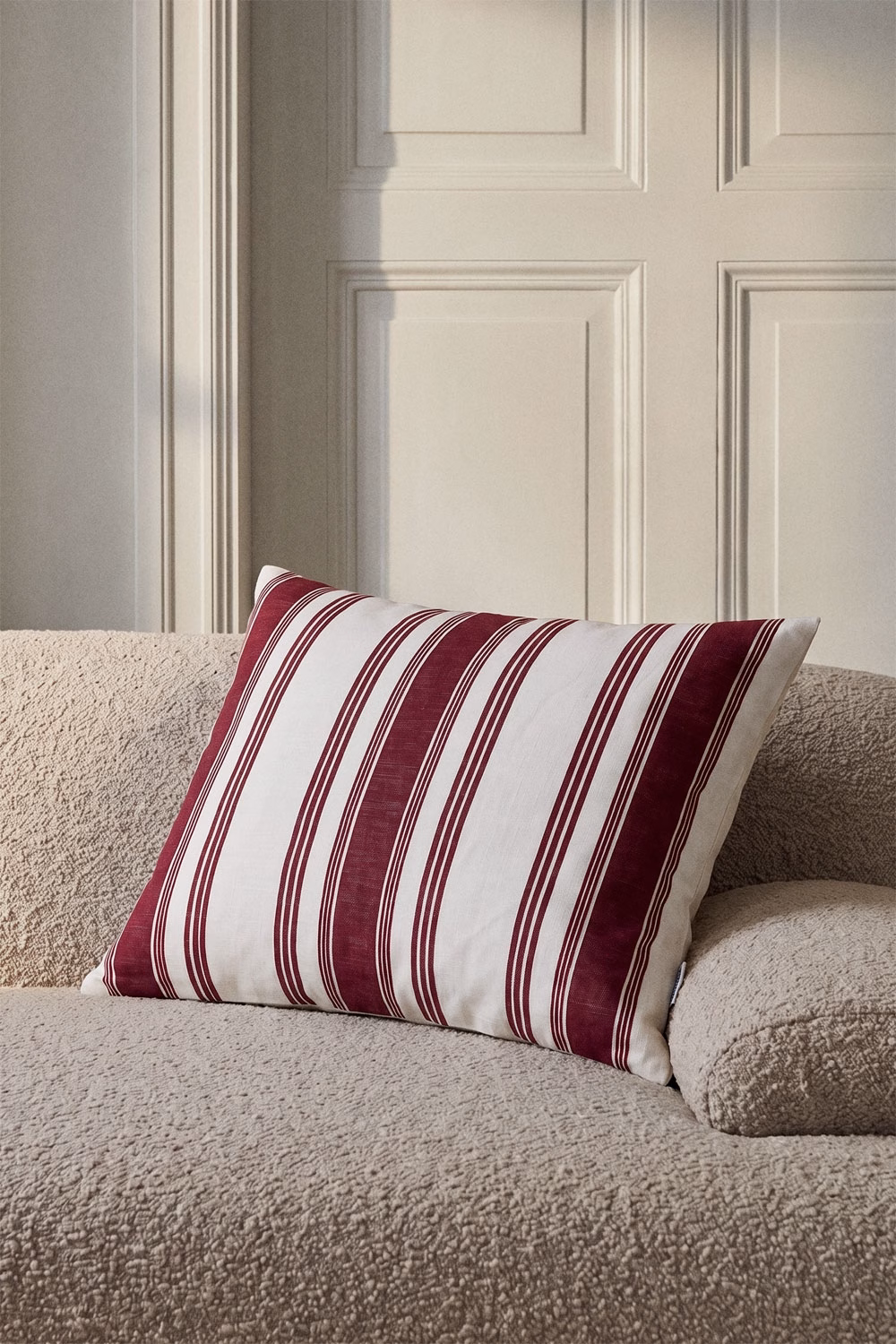 Coussin à rayures bordeaux et blanches sur une base neutre, idéal pour ajouter du dynamisme visuel à un canapé beige.