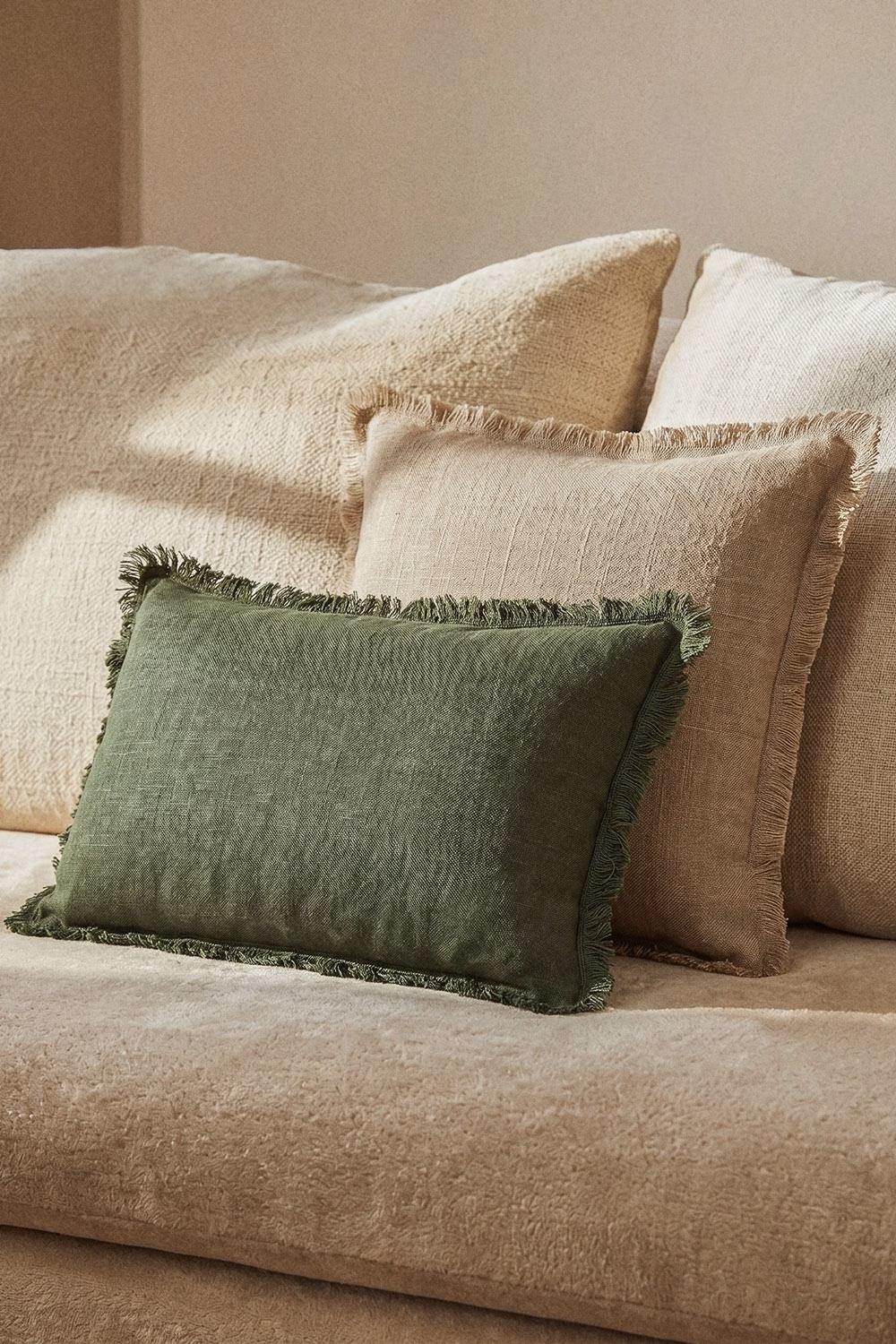 Coussin vert à franges en lin rustique posé sur un canapé beige, idéal pour créer un contraste de textures naturel.